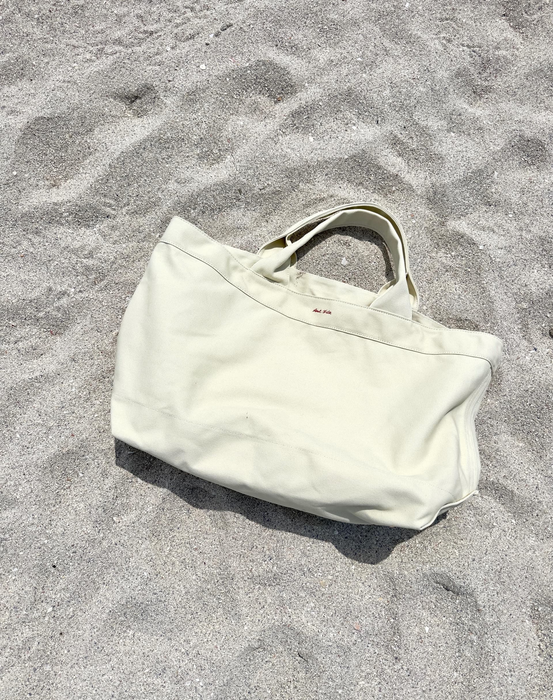 Extra-large canvas beach tote on sand - oversized luxury carryall with silver base studs
